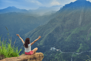 Traveler raising arms in awe atop a scenic viewpoint with lush valleys and winding roads below capturing the adventure and beauty of Ella Rock or Little Adam’s Peak in Sri Lanka.