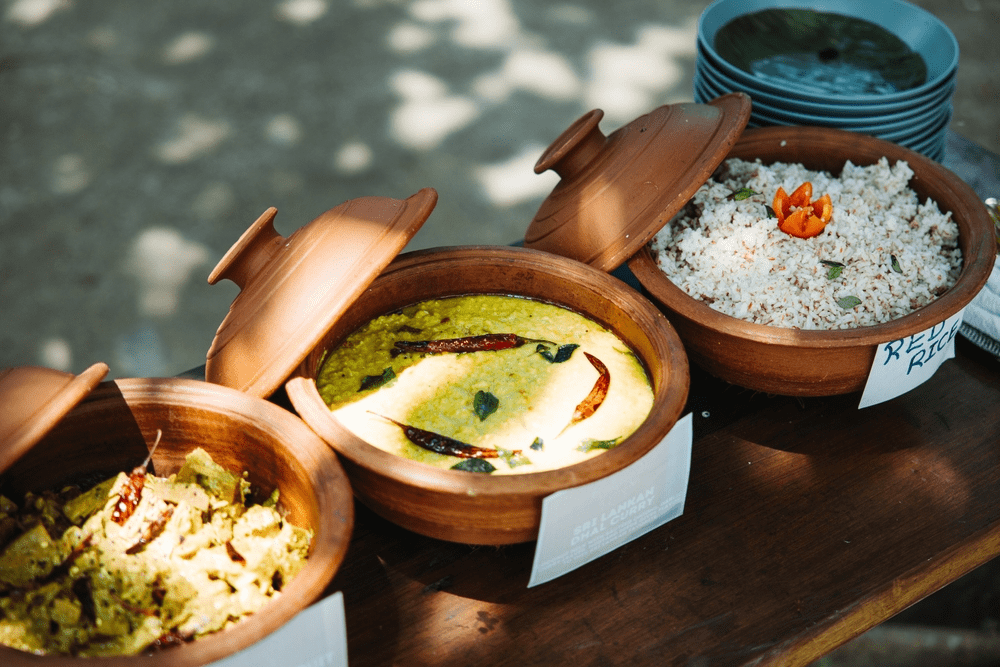 Traditional Sri Lankan food served in clay pots with curry and rice dishes on a wooden table outdoors.