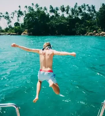 Adventurer diving off a boat into clear waters near Sri Lanka, a thrilling Islandwyde trip by travel agents in Colombo, Sri Lanka